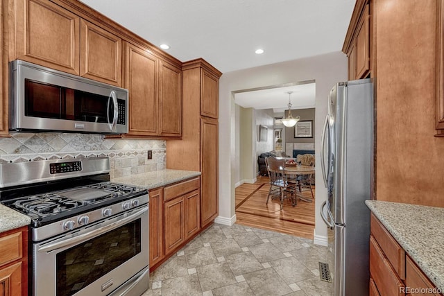 kitchen with backsplash, light stone countertops, brown cabinets, and appliances with stainless steel finishes