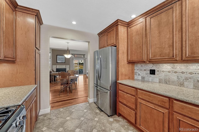 kitchen featuring brown cabinets, stone finish floor, appliances with stainless steel finishes, decorative backsplash, and light stone countertops