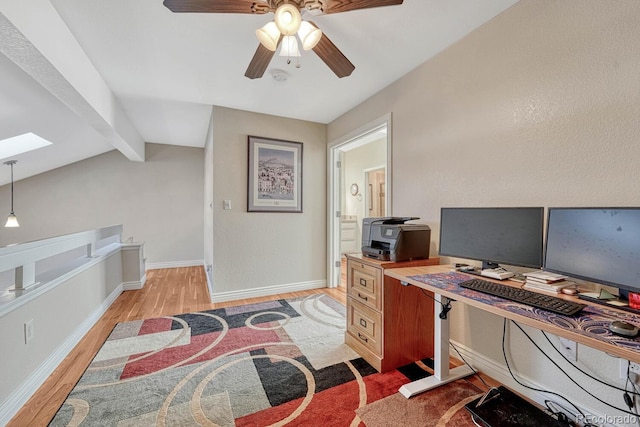 office space with light wood finished floors, ceiling fan, lofted ceiling with skylight, and baseboards