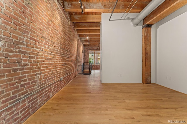 hall with beamed ceiling, brick wall, and light hardwood / wood-style flooring