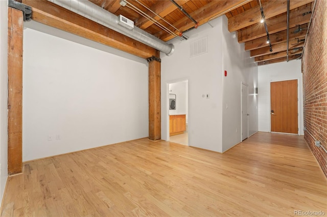 unfurnished room featuring wooden ceiling, brick wall, a towering ceiling, and light wood-type flooring