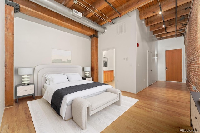 bedroom featuring ensuite bath, a towering ceiling, beamed ceiling, light wood-type flooring, and wooden ceiling