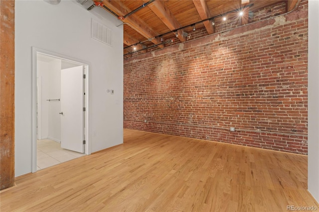 empty room featuring light hardwood / wood-style floors, beamed ceiling, brick wall, and wood ceiling