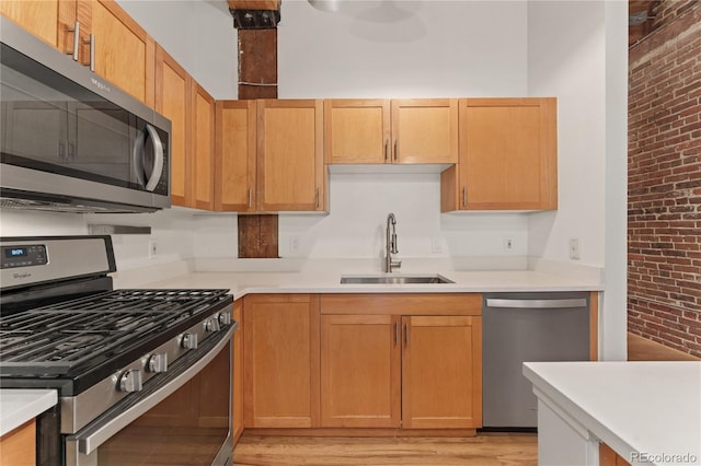 kitchen featuring sink, brick wall, light hardwood / wood-style flooring, and appliances with stainless steel finishes