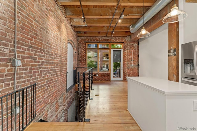 corridor with light hardwood / wood-style floors, brick wall, beam ceiling, and a towering ceiling