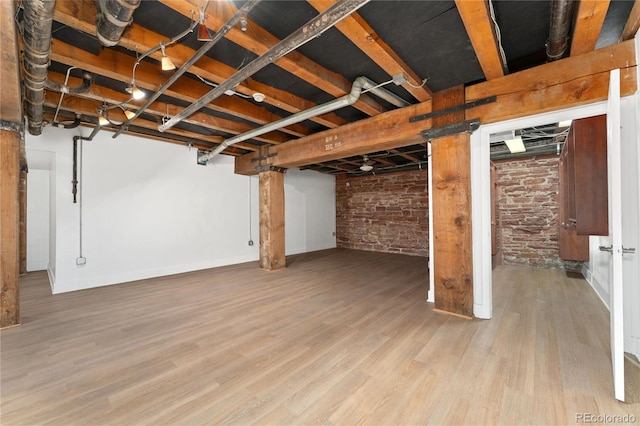 basement featuring light wood-type flooring and brick wall