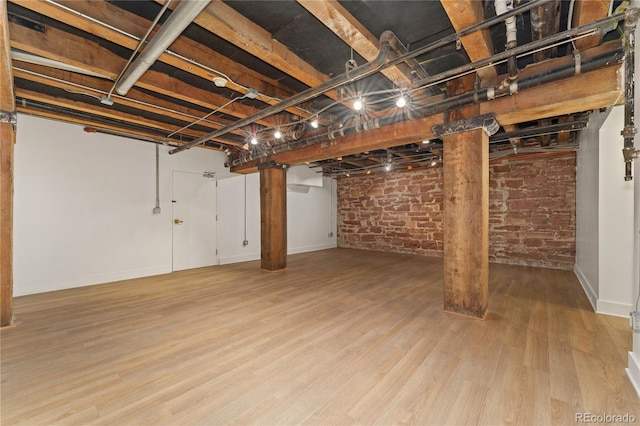 basement featuring brick wall and light hardwood / wood-style flooring