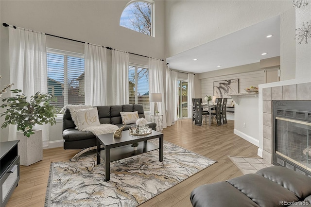 living room featuring a towering ceiling, a tiled fireplace, and light hardwood / wood-style floors