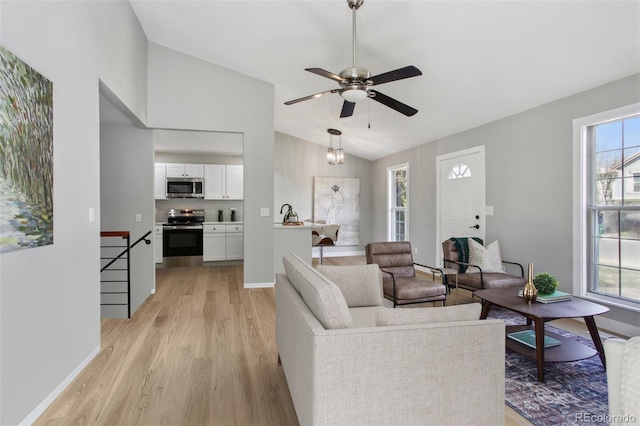 living area featuring vaulted ceiling, light wood finished floors, ceiling fan, and baseboards