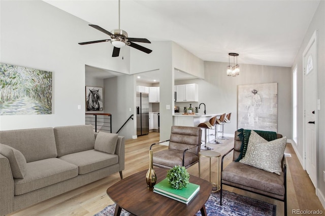 living area featuring light wood finished floors, lofted ceiling, a chandelier, ceiling fan, and baseboards