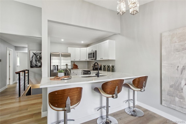 kitchen with stainless steel appliances, a sink, light wood-style floors, a breakfast bar area, and white cabinets
