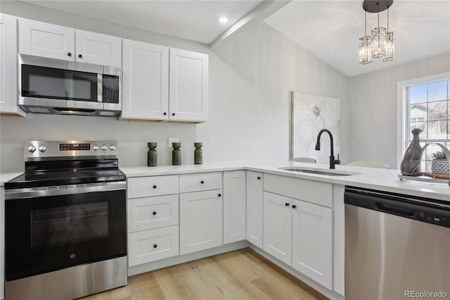 kitchen with a sink, stainless steel appliances, white cabinets, light countertops, and light wood-style floors