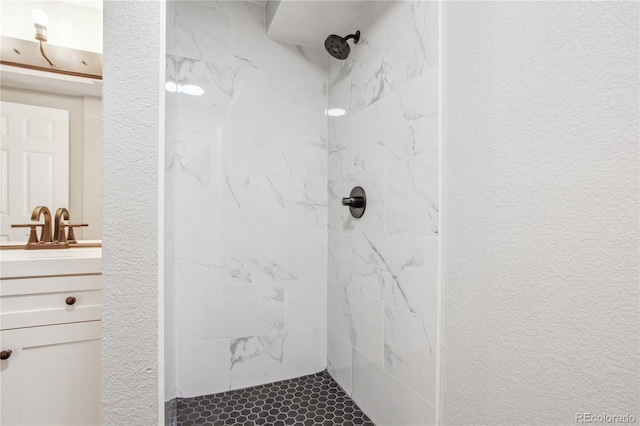 bathroom with vanity, a tile shower, and a textured wall