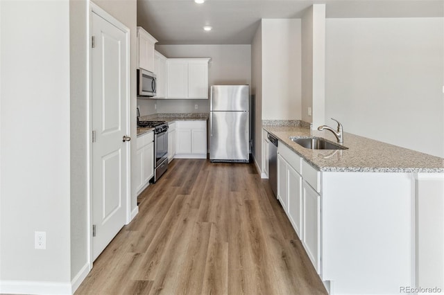 kitchen featuring sink, light stone countertops, light wood-type flooring, white cabinetry, and stainless steel appliances