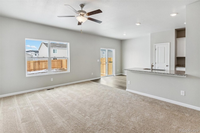 unfurnished living room featuring ceiling fan, light colored carpet, and sink