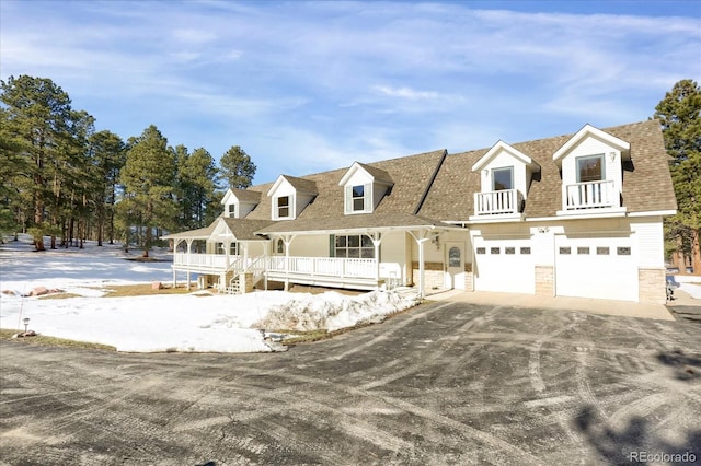 cape cod-style house featuring covered porch, a balcony, and a garage