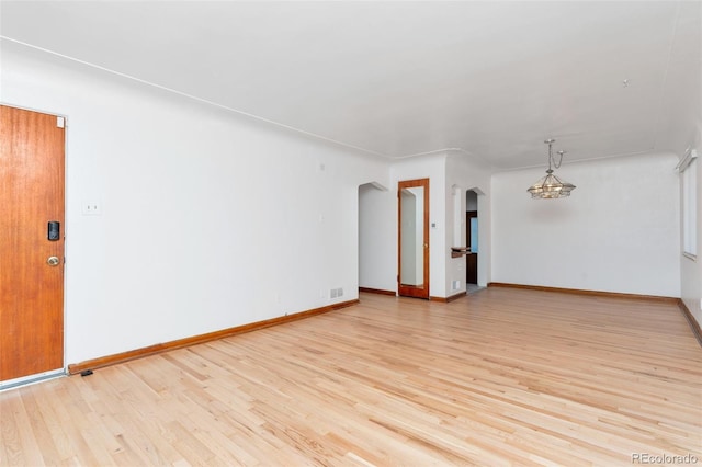 empty room featuring arched walkways, visible vents, an inviting chandelier, light wood-style floors, and baseboards