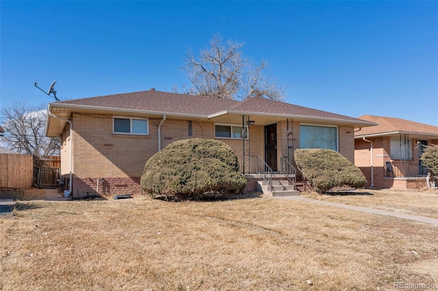 ranch-style house featuring a shingled roof, fence, a front lawn, and brick siding