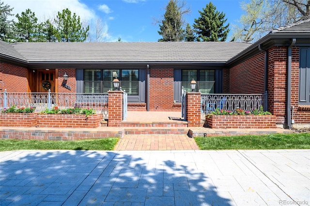view of front of home featuring a tiled roof, a porch, and brick siding