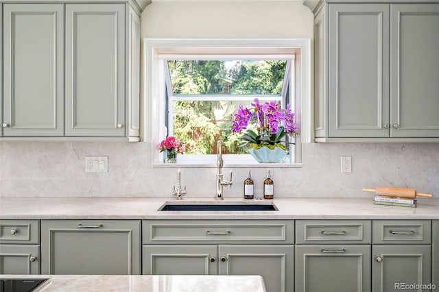 kitchen with a sink, decorative backsplash, light stone countertops, and gray cabinetry