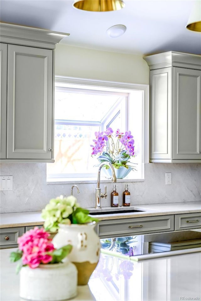 kitchen with a sink, gray cabinets, backsplash, and light countertops