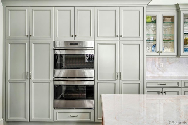 kitchen featuring glass insert cabinets, light stone counters, and stainless steel double oven