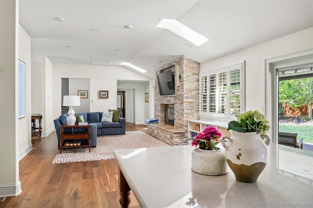 living room with baseboards, wood finished floors, vaulted ceiling with skylight, and a fireplace
