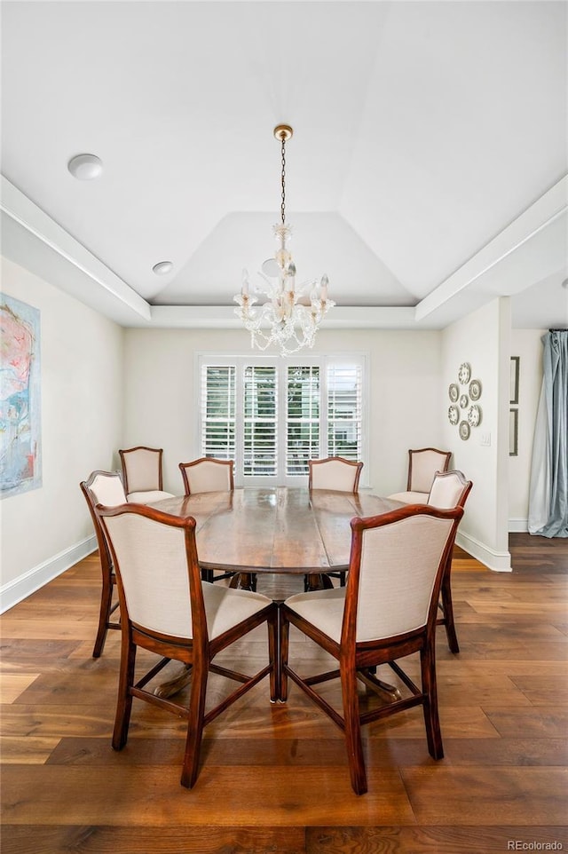 dining space featuring baseboards, a tray ceiling, an inviting chandelier, and wood finished floors