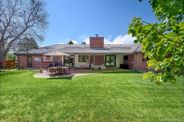 back of property featuring a lawn, a patio, a chimney, and brick siding