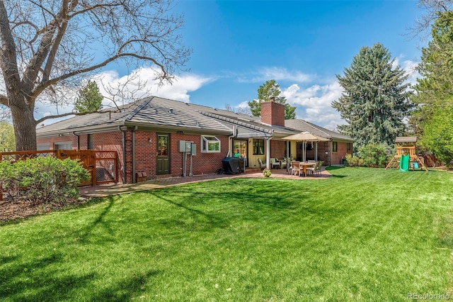 rear view of property with brick siding, a chimney, a playground, a patio, and a yard