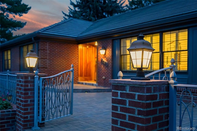 exterior entry at dusk featuring brick siding, a gate, and a tile roof