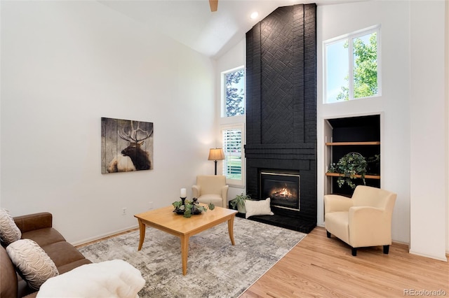 living room with built in shelves, a large fireplace, high vaulted ceiling, and light hardwood / wood-style floors