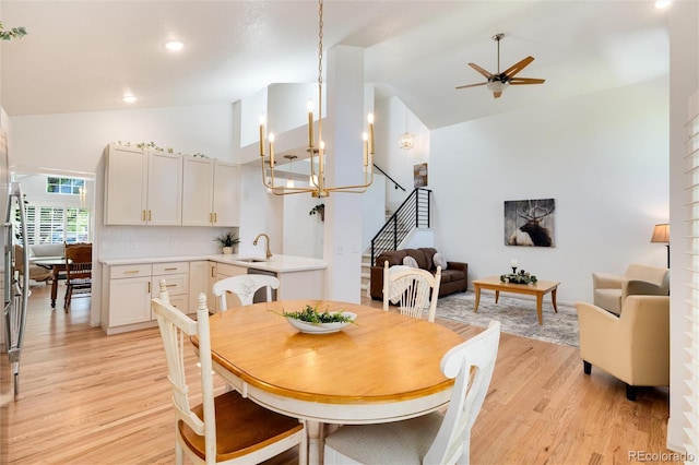 dining area featuring ceiling fan with notable chandelier, light wood-type flooring, high vaulted ceiling, and sink