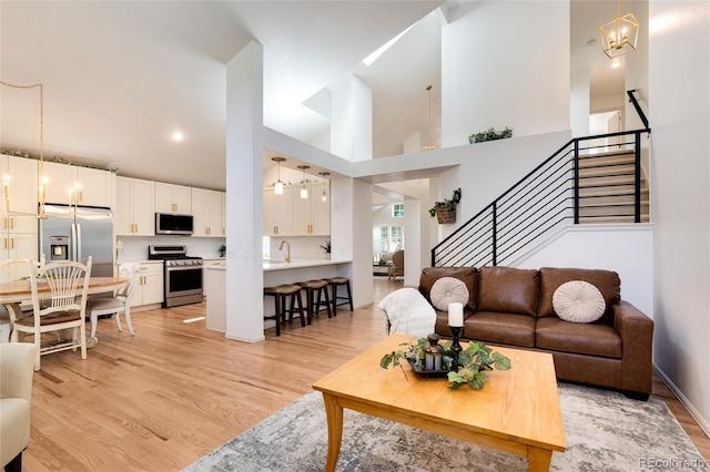 living room with a high ceiling, light wood-type flooring, an inviting chandelier, and sink