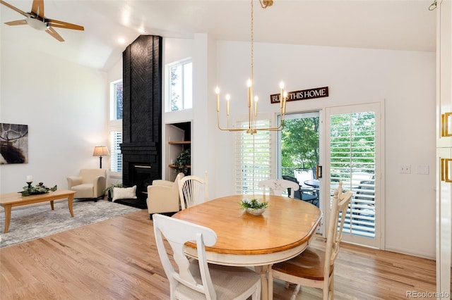 dining area with plenty of natural light, light wood-type flooring, ceiling fan with notable chandelier, and a brick fireplace