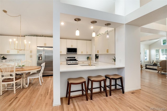 kitchen featuring kitchen peninsula, stainless steel appliances, decorative light fixtures, light hardwood / wood-style floors, and white cabinetry