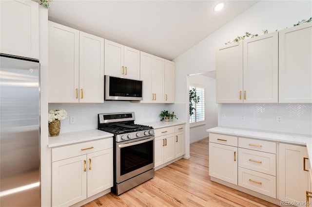 kitchen featuring appliances with stainless steel finishes, white cabinetry, vaulted ceiling, and light hardwood / wood-style flooring