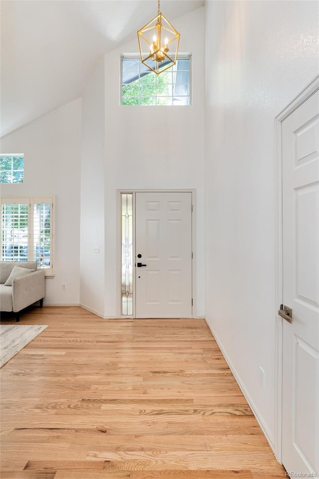 entryway with a notable chandelier, high vaulted ceiling, and light hardwood / wood-style flooring