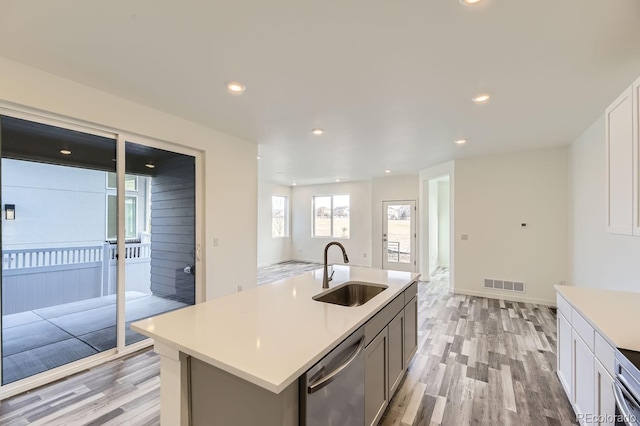 kitchen featuring dishwasher, sink, a center island with sink, and light wood-type flooring