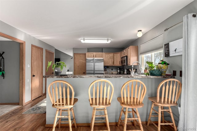 kitchen with kitchen peninsula, hardwood / wood-style floors, a breakfast bar, and appliances with stainless steel finishes