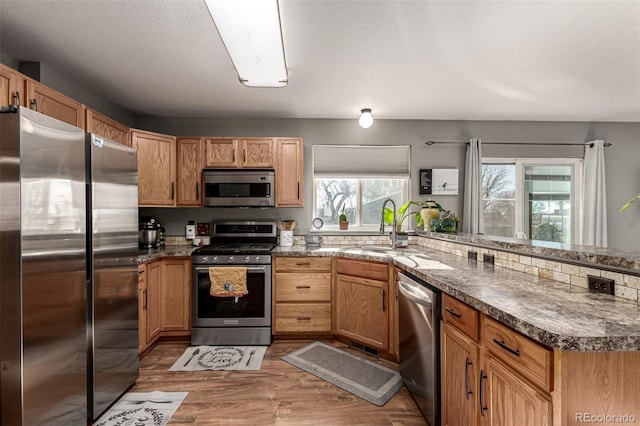 kitchen with kitchen peninsula, sink, a textured ceiling, appliances with stainless steel finishes, and wood-type flooring