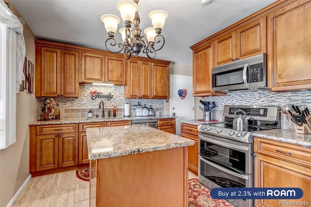 kitchen featuring an inviting chandelier, sink, light stone countertops, appliances with stainless steel finishes, and a kitchen island