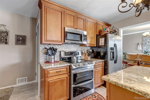 kitchen featuring a notable chandelier, light stone counters, decorative backsplash, and stainless steel appliances