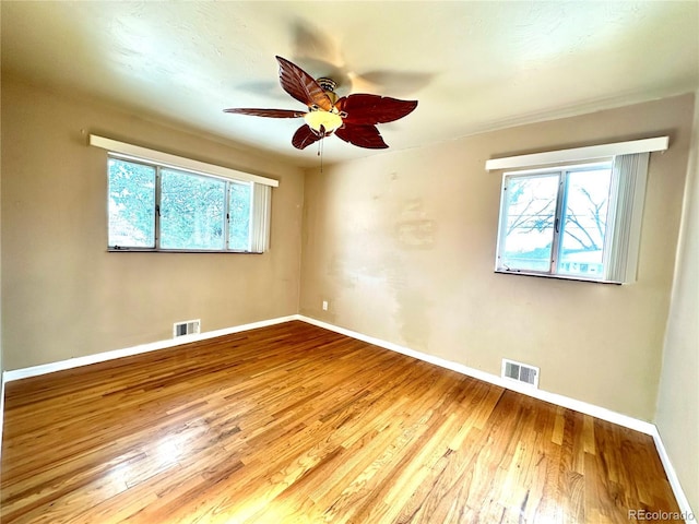 empty room with ceiling fan, hardwood / wood-style floors, and a healthy amount of sunlight