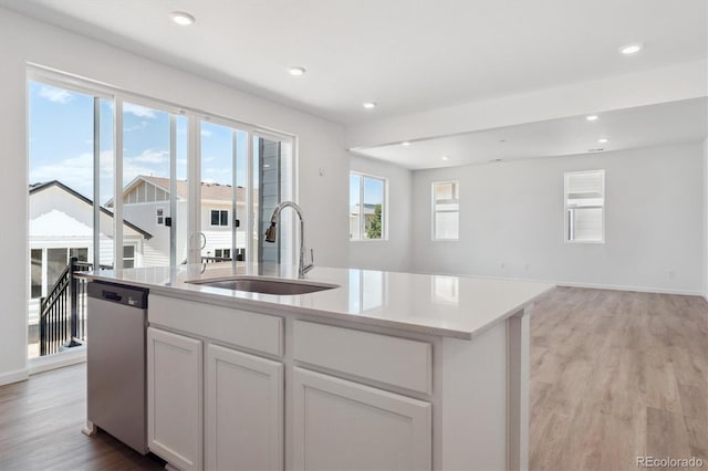 8339 Snake River St, Littleton, CO 80125 - kitchen with stainless steel dishwasher, open floor plan, an island with sink, light wood-style floors, and white cabinets