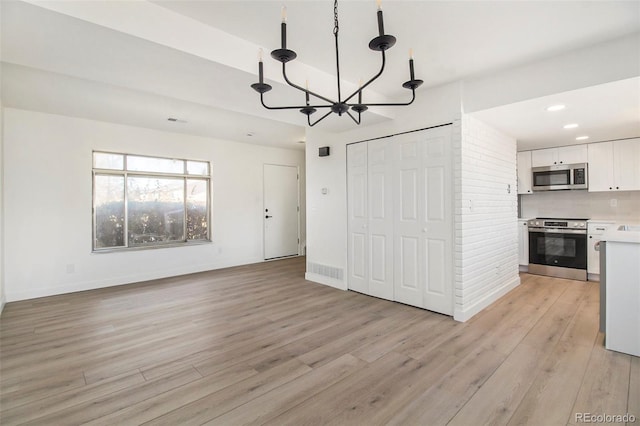 interior space featuring white cabinets, pendant lighting, stainless steel appliances, and light hardwood / wood-style floors