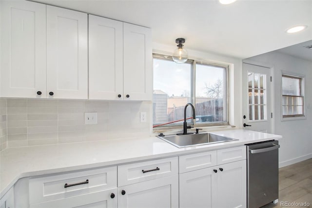 kitchen with white cabinetry, sink, stainless steel dishwasher, decorative backsplash, and light wood-type flooring