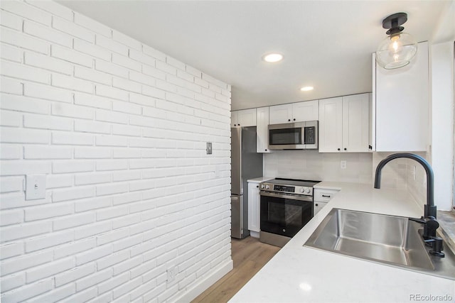 kitchen featuring sink, light hardwood / wood-style flooring, decorative backsplash, white cabinets, and appliances with stainless steel finishes