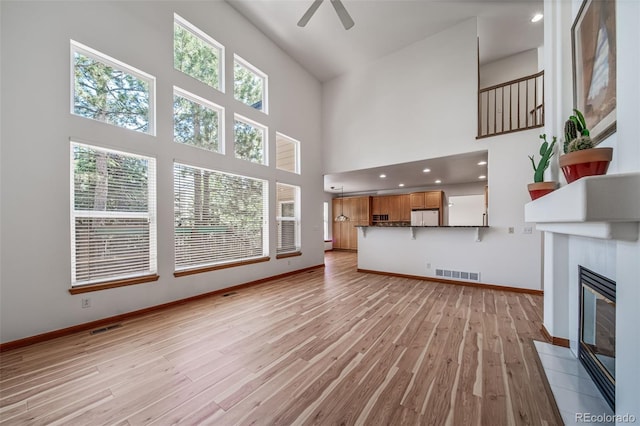 5416 S Hannibal Ct, Centennial, CO 80015 - unfurnished living room with a high ceiling, light wood-style flooring, ceiling fan, and a tiled fireplace