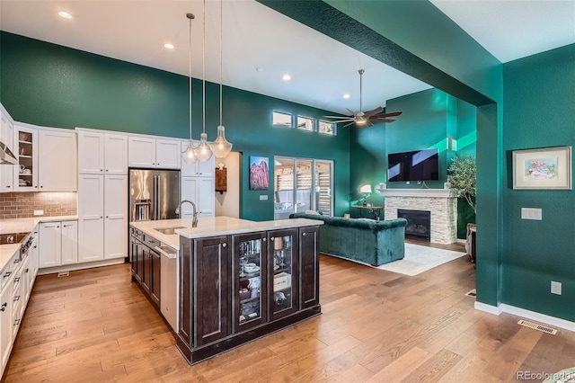 kitchen featuring glass insert cabinets, visible vents, open floor plan, light countertops, and a center island with sink